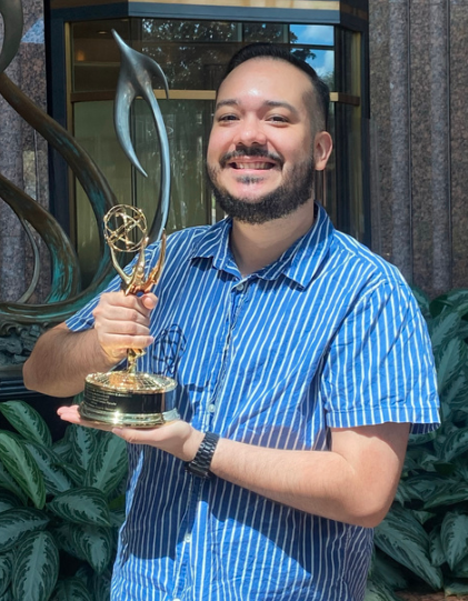 A person posing with an Emmy Award